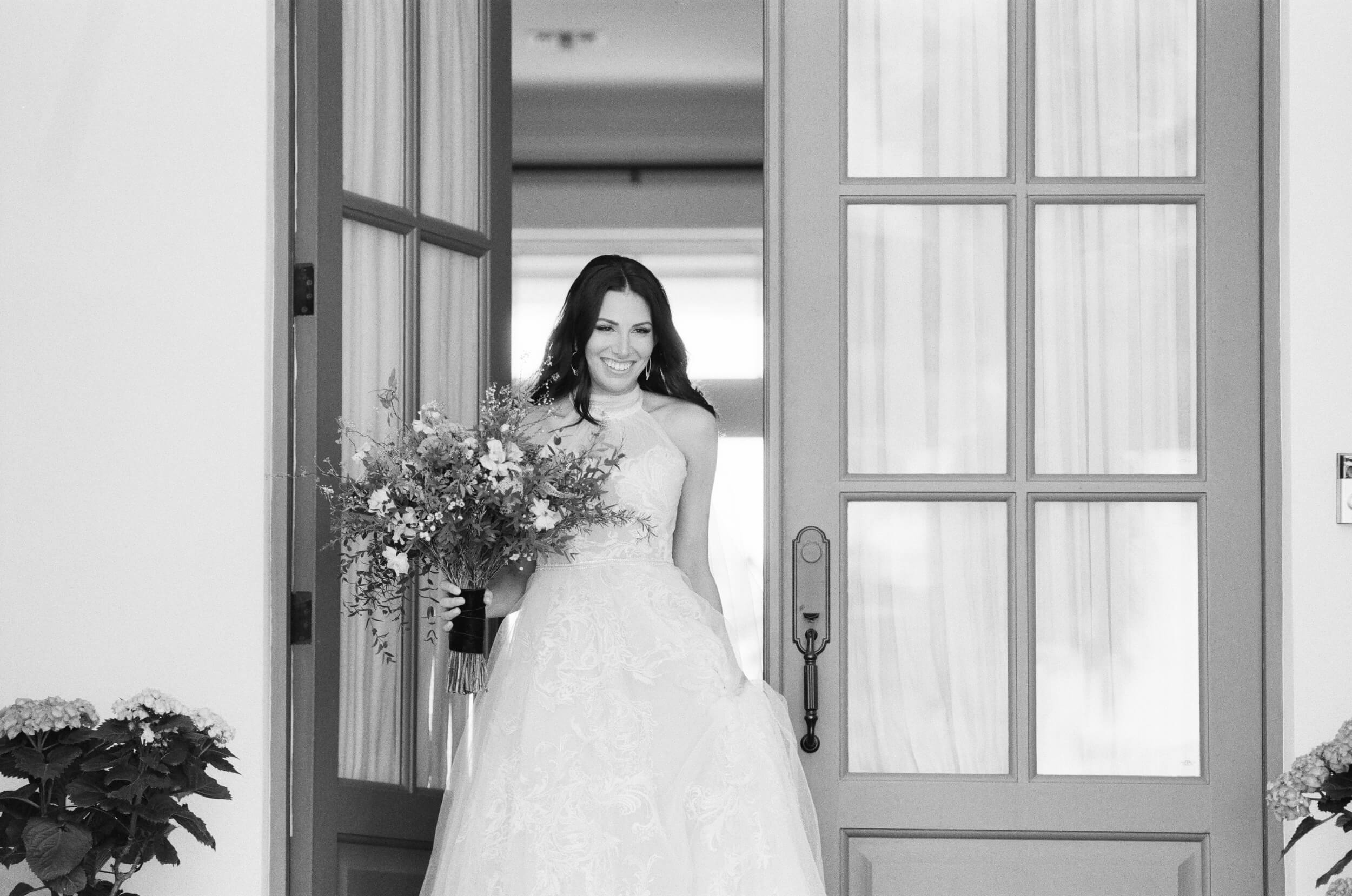 bride coming out of house with bouquet
