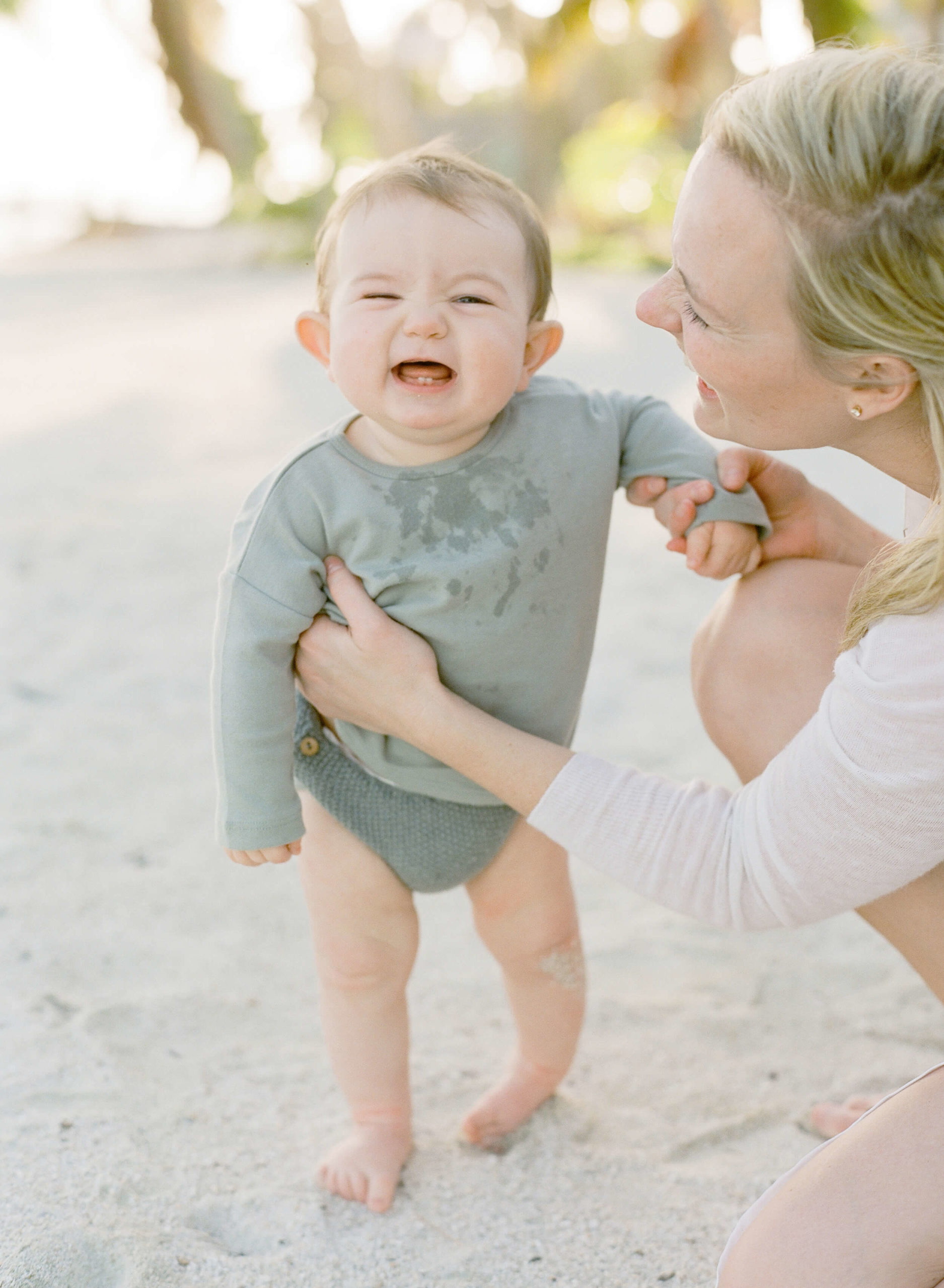 baby boy laughing with  mother on the beach