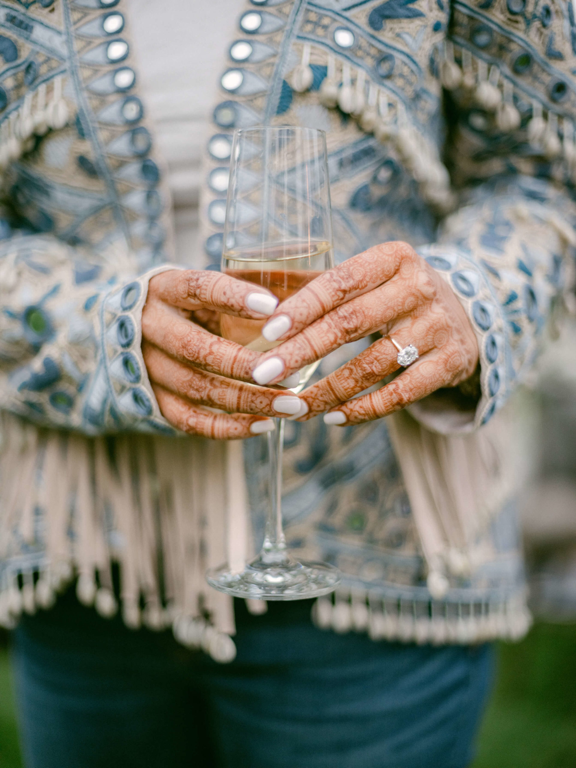 Closeup of Sapna's henna'd hands holding a glass of champagne