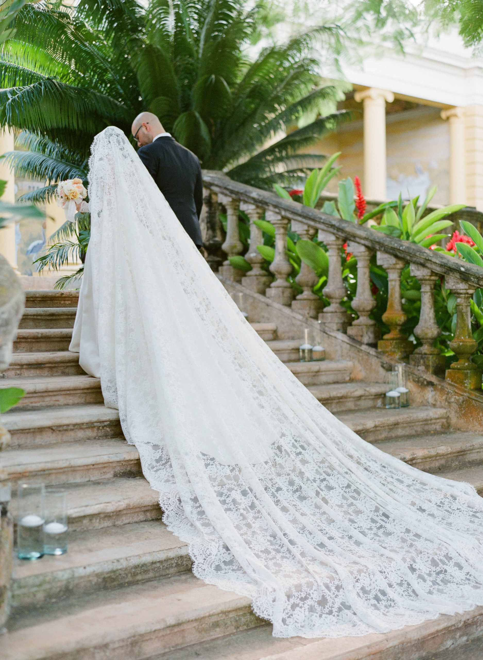Bride and groom walk up stairs with veil trailing behind