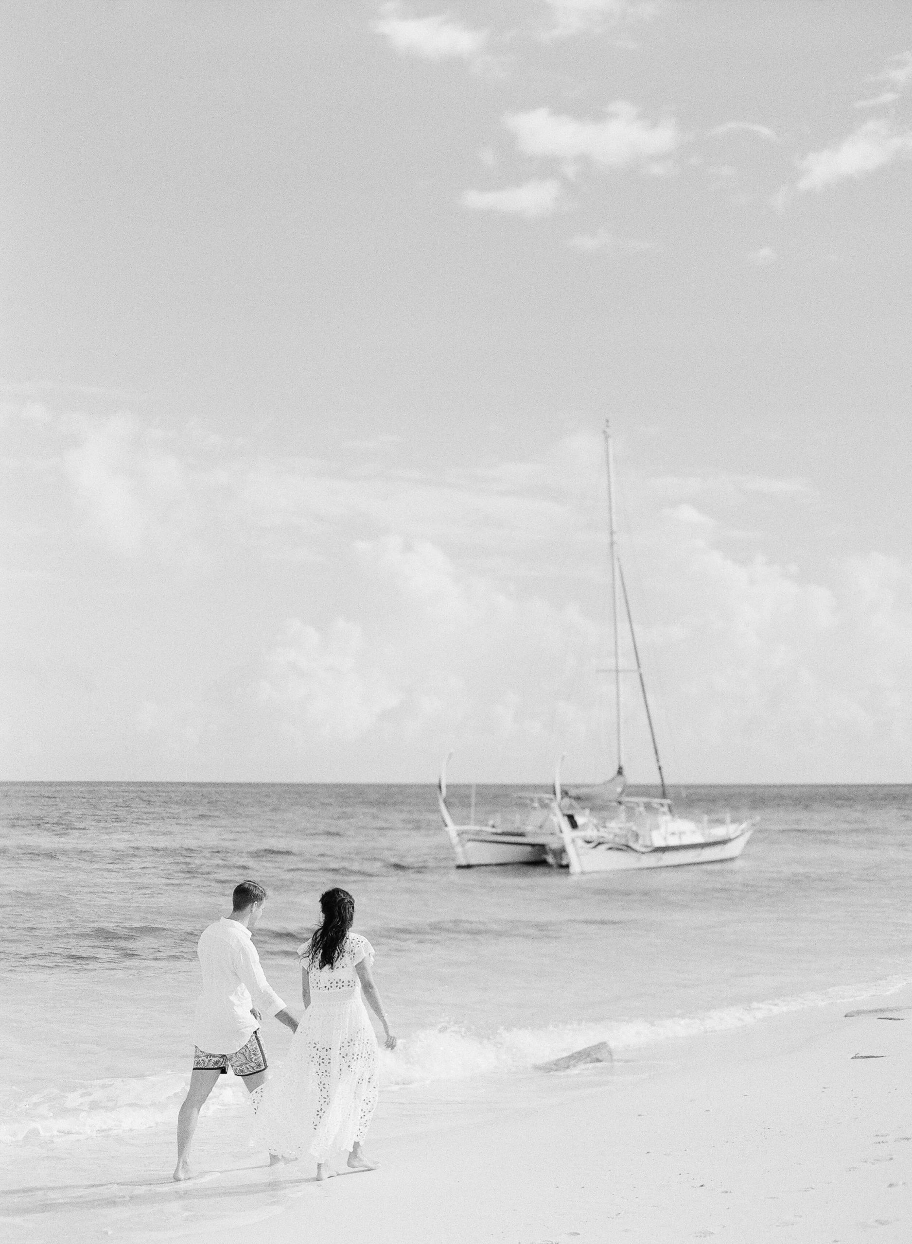 Liz and Dave walking along the beach with a boat in the background