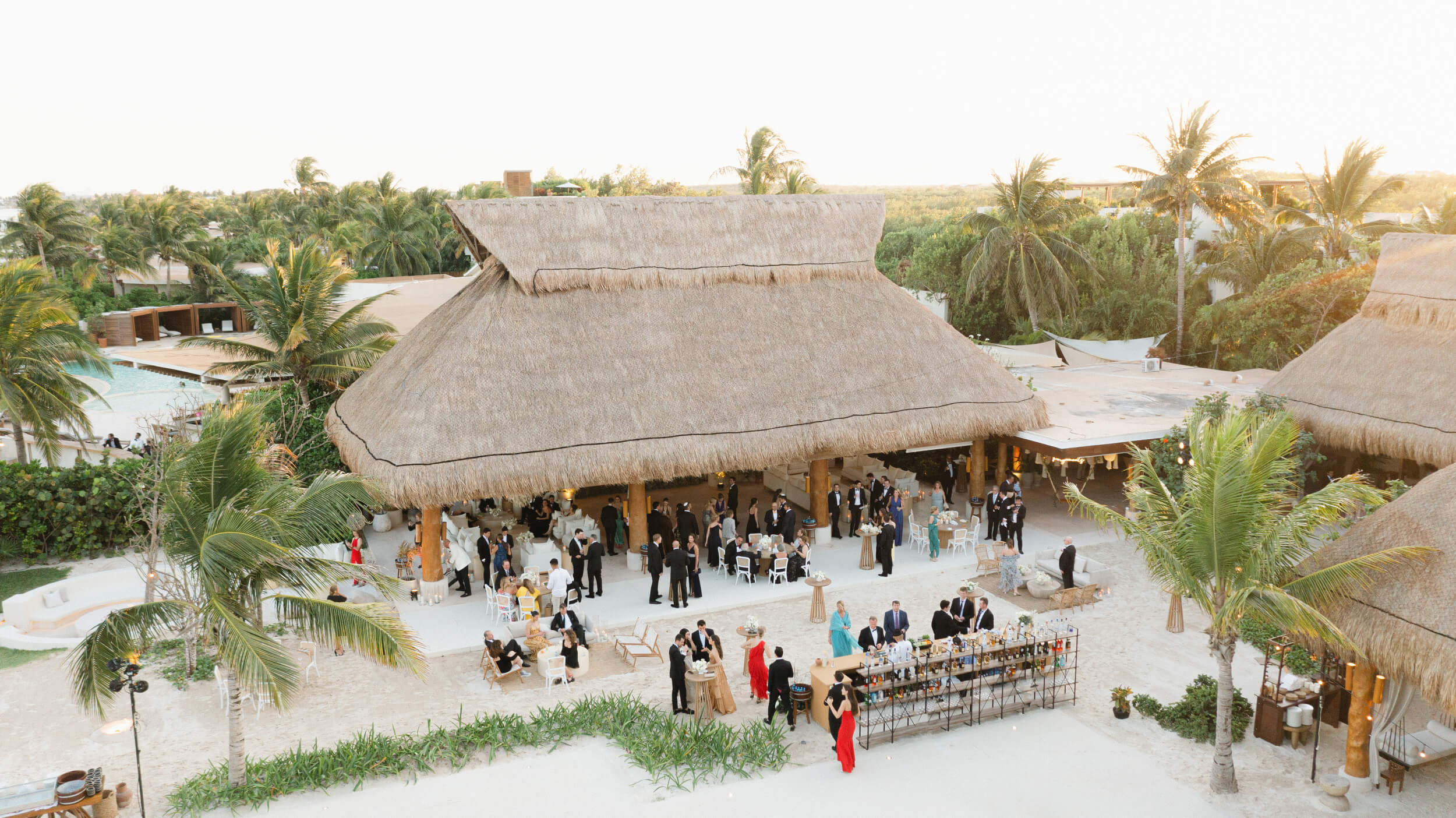 Guests gather under a tiki surrounded by palm trees at Danielle and Lucas' Rosewood Mayakoba wedding in Playa del Carmen