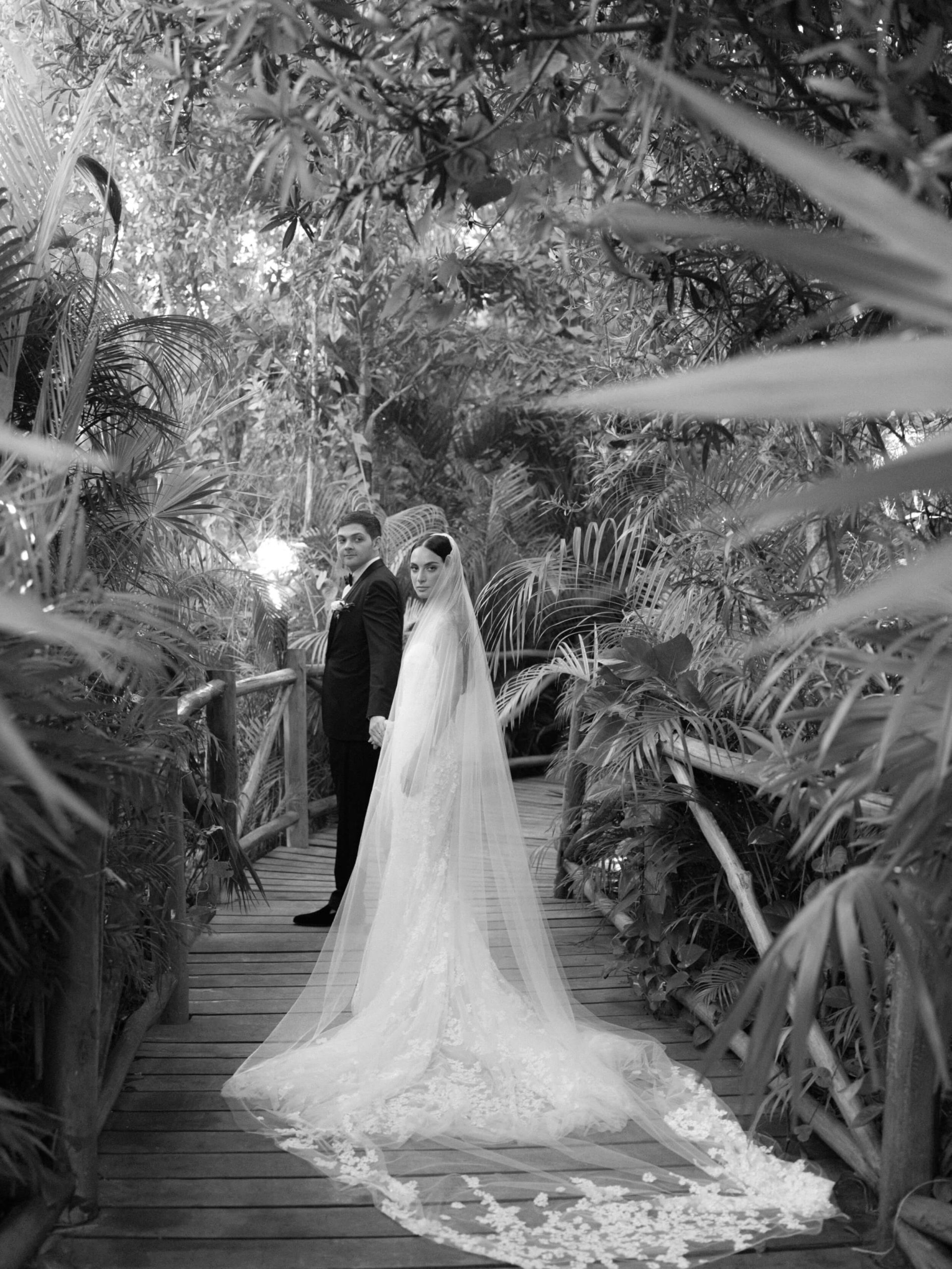 Danielle and Lucas posing under the trees on a boardwalk after their wedding at the Rosewood Mayakoba Resort