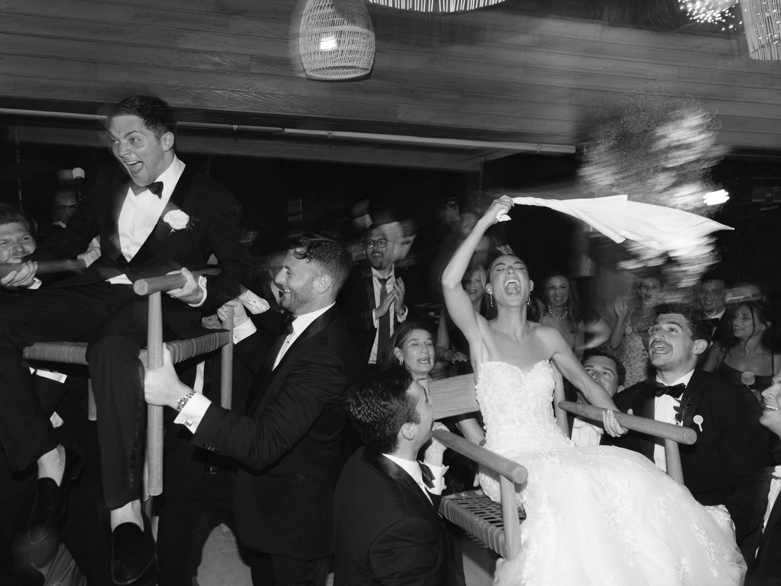 Danielle and Lucas laughing while being lifted into the air on chairs during 'hora', a Jewish wedding tradition