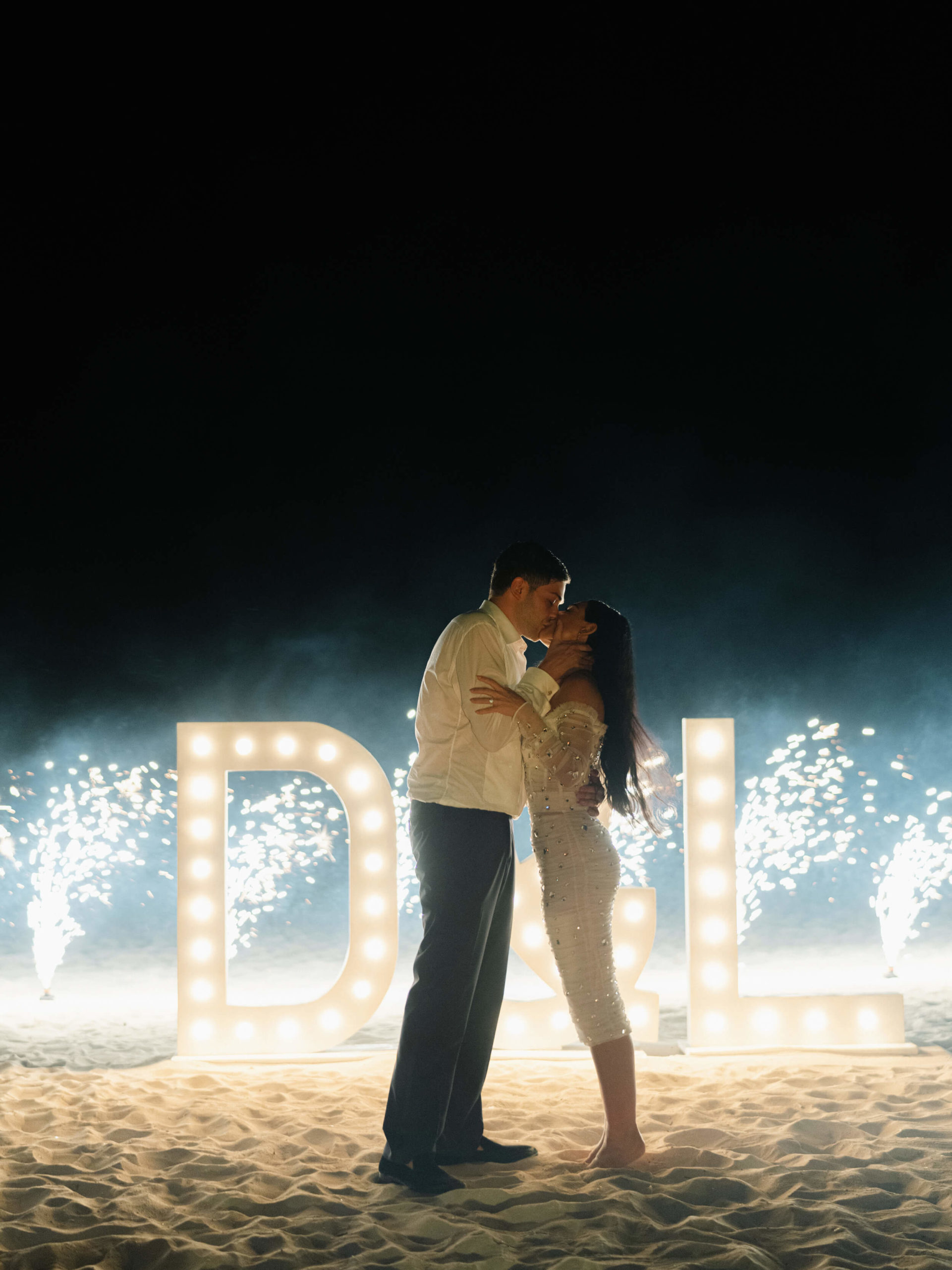 Danielle and Lucas kissing in front of lighted letters that say "D & L"