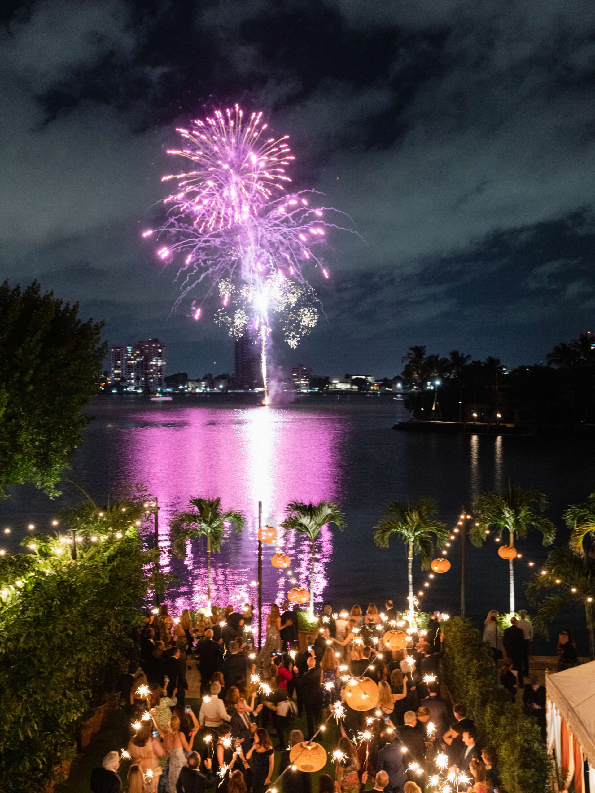 Fireworks display over the water as guests look on