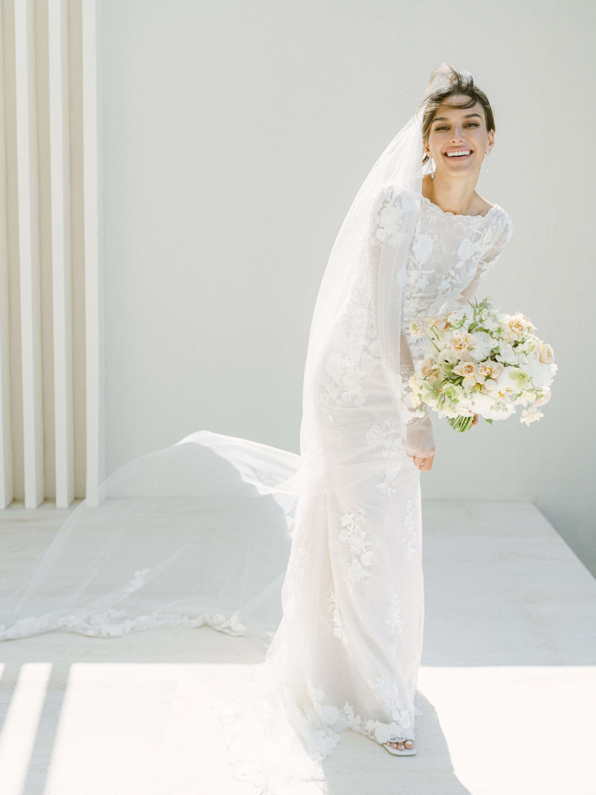 Olga laughing in her wedding gown, veil, holding her bouquet, wind blowing