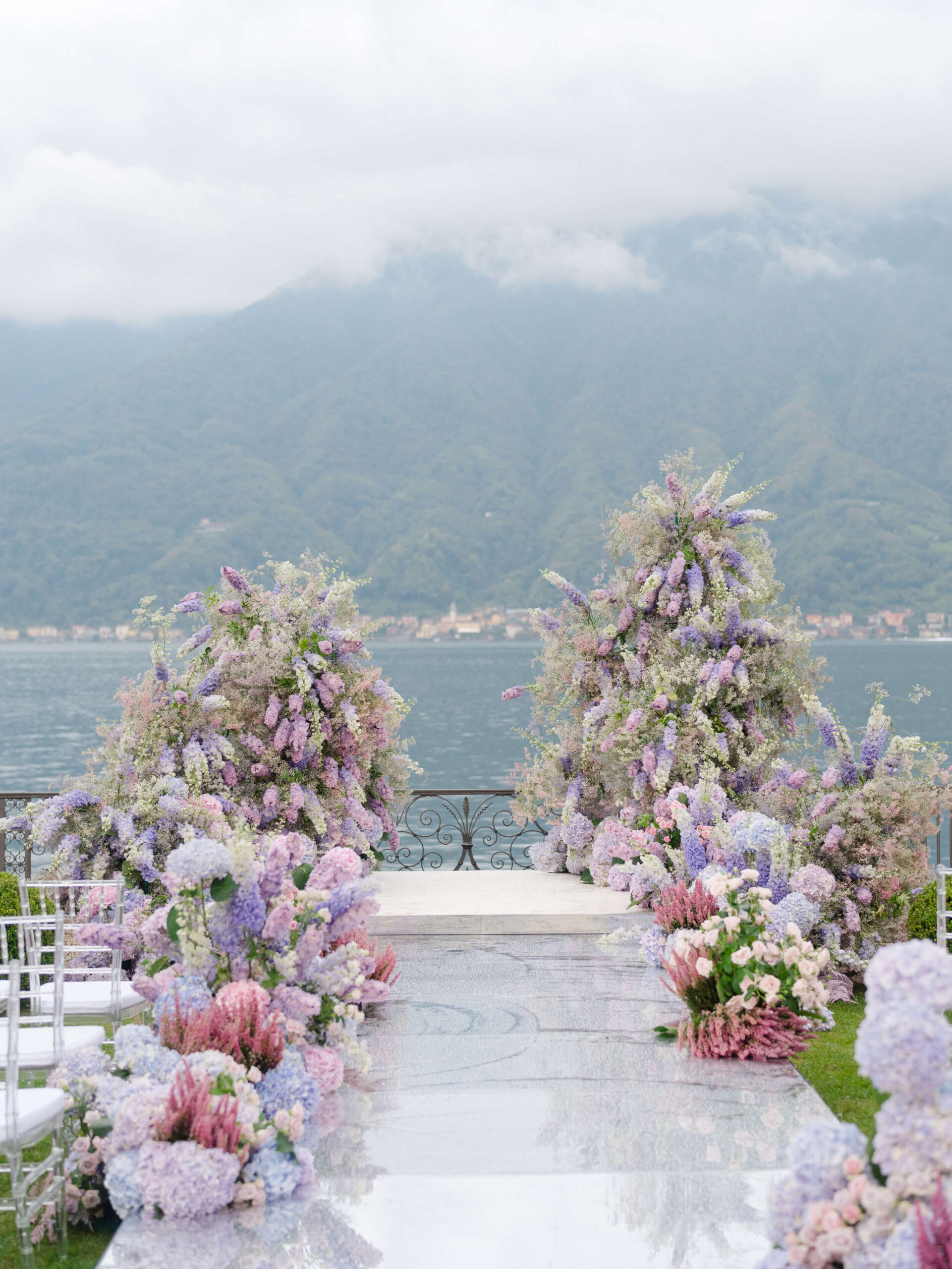Wedding aisle lined with a cascade of purple delphiniums; the mountains of Lake Como in the distance; clouds overhead