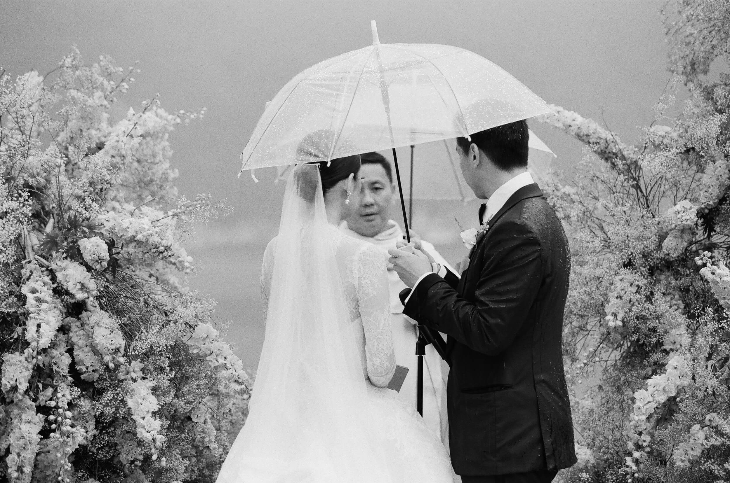 Black and white shot of bride and groom under an umbrella at their wedding ceremony